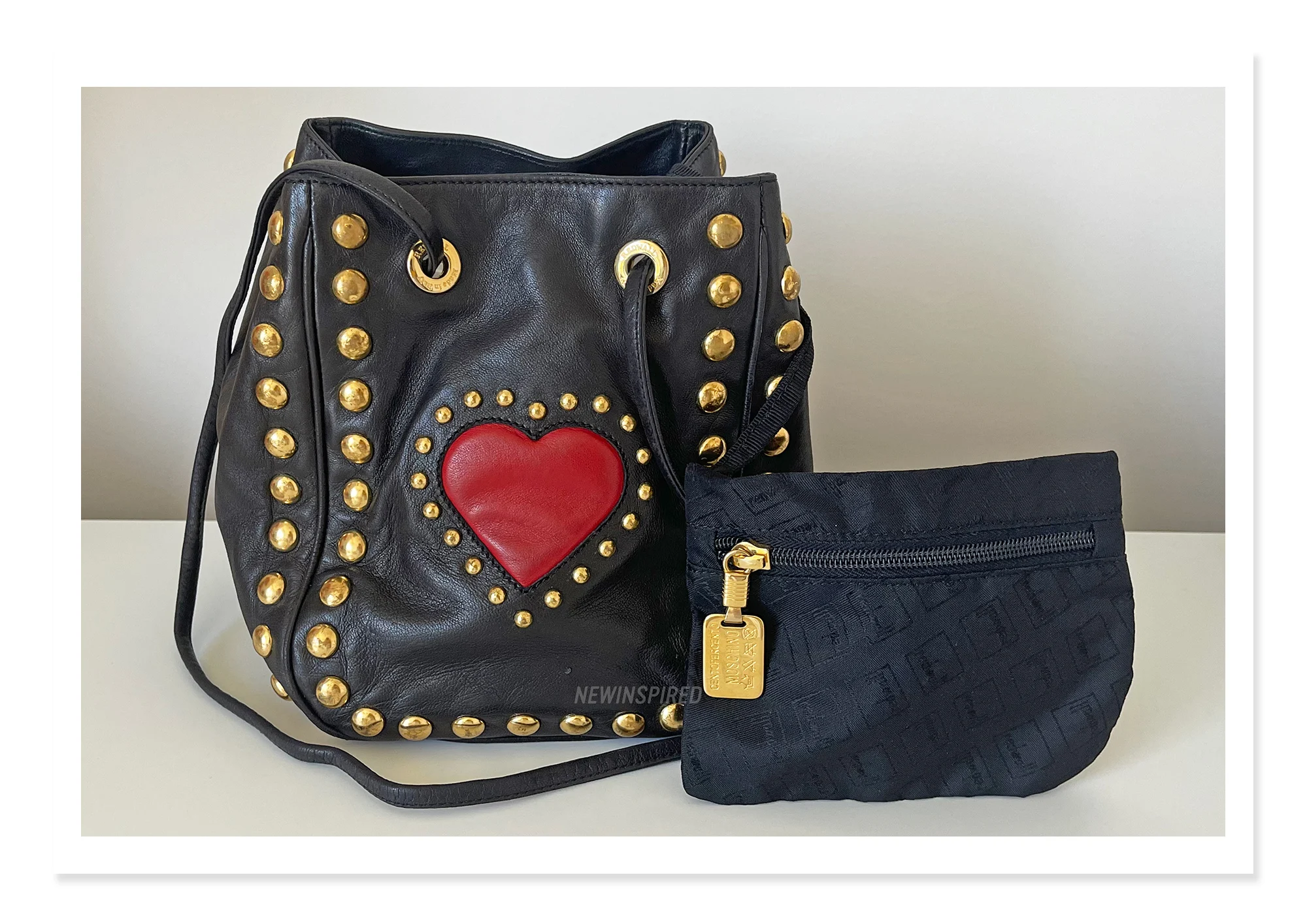 A black bucket bag with gold studs around the edges and a red heart in the center and a pouch